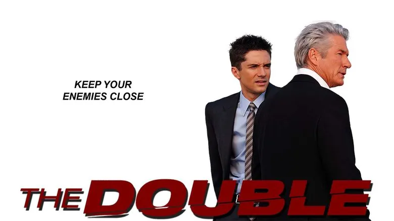 Simon James stands bewildered as his doppelganger, James Simon, confidently interacts with others in the office, a stark visible contrast between their demeanors.